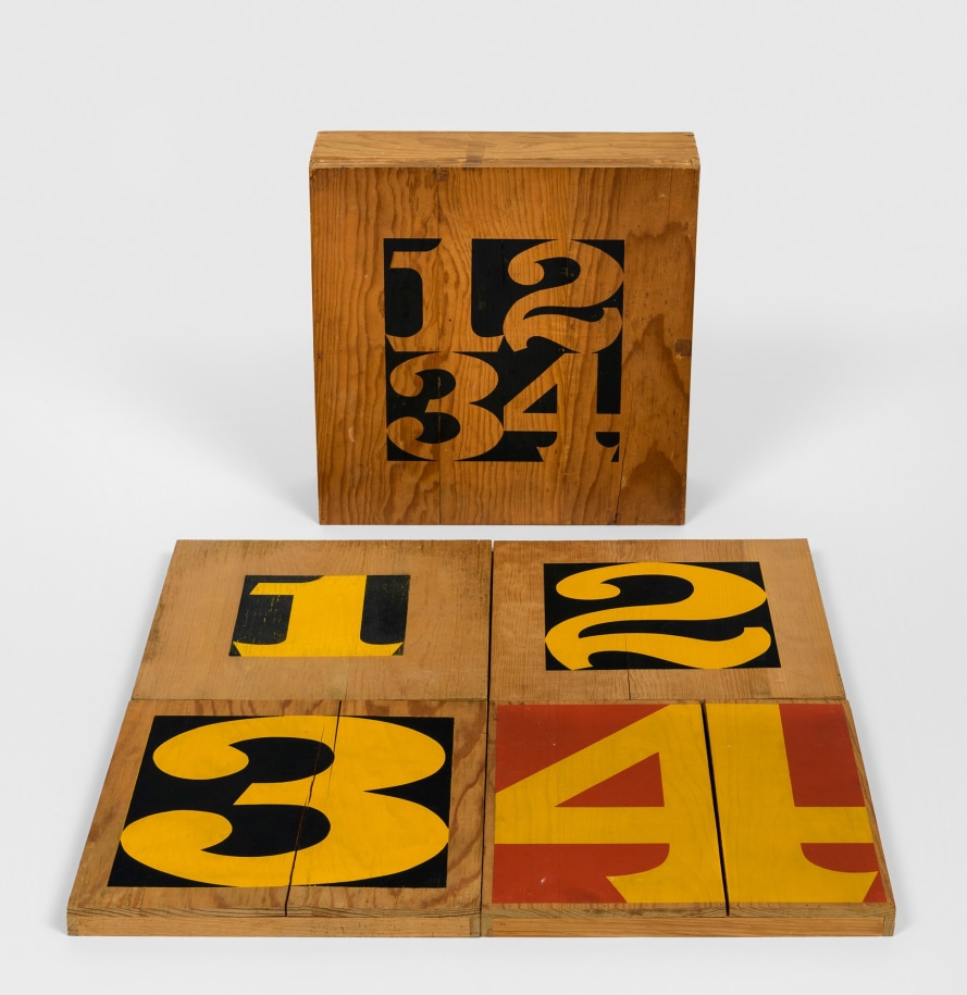 A wooden box holding four individual wooden numbers. The numbers one, two, and three consist of a yellow numeral in a black square background. The number four is a yellow numeral four in a red square background.. The numbers get progressively bigger.