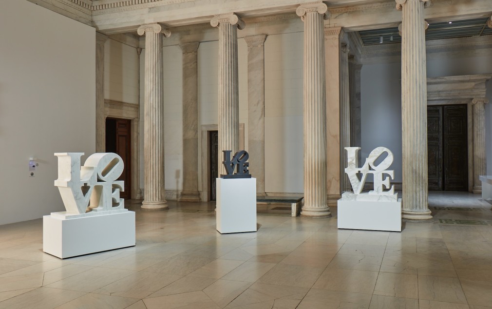 Installation view of Robert Indiana: A Sculpture Retrospective at the Albright-Knox Gallery of Art, featuring two white and one black marble LOVE sculptures.