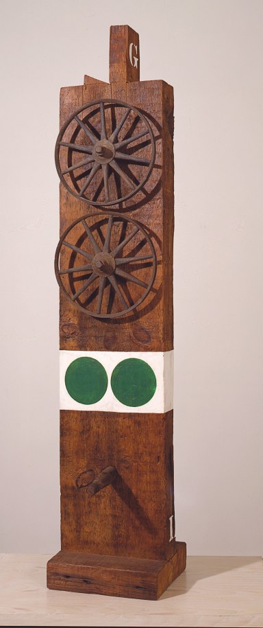 Ge, a wooden sculpture measuring 58 1/2 by 12 by 14 inches that consists of a wooden beam with a haunched tenon on a wooden base. On the top front of the sculpture are two iron and wooden wheels. Below the wheels is a white band of paint with two green circles. Halfway below the white band and the base a wooden peg protrudes from the sculpture.
