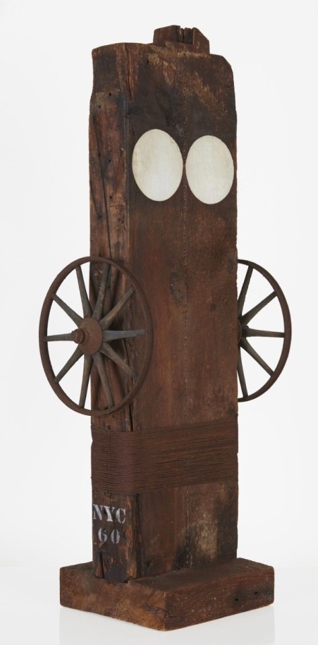 Virgin, a 42 1/2 sculpture consisting of a wooden beam with a haunched tenon on a wooden base. Two white circles are painted on the front of the sculpture, near the top. An iron wheel has been attached to the middle of the left and right sides of the sculpture, and wire has been wrapped around the work below the wheels.