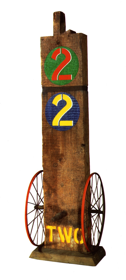 A 62 1/2 by 19 by 20 inch sculpture consisting of a wooden beam with a haunched tenon on a wooden base. The work's title, &quot;Two,&quot; is painted in yellow stenciled letters across the bottom front of the sculpture. An iron wheel is attached to the bottom left and right sides of the sculpture, and a wooden peg has been affixed to the front of the sculpture, in between the wheels. At the top of the sculpture is a green circle with a red numeral two, and below that is a blue circle with a yellow numeral two.