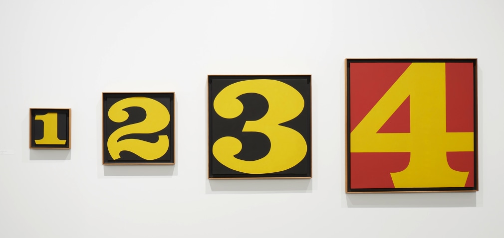 Exploding Numbers, a painting consisting of four canvases, the smallest, 12 inches square, consists of a yellow numeral one against a black ground. The second panel is 24 inches square and consists of a yellow numeral two against a black ground; the third panel is 36 inches square with a yellow numeral three against a black ground, the last panel is 48 inches square with a yellow numeral four against a red ground.
