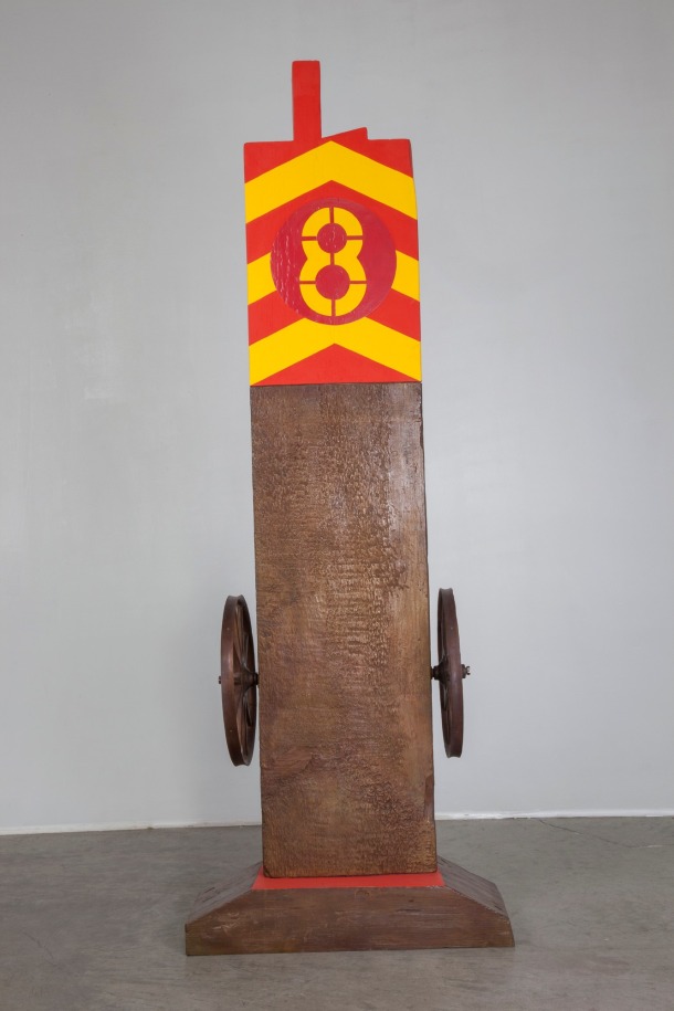 The verso of the bronze herm Chief. Red and yellow danger stripes occupy the top third of the verso. In the center of the danger stripes is a yellow numeral &quot;8&quot; in a red circle.