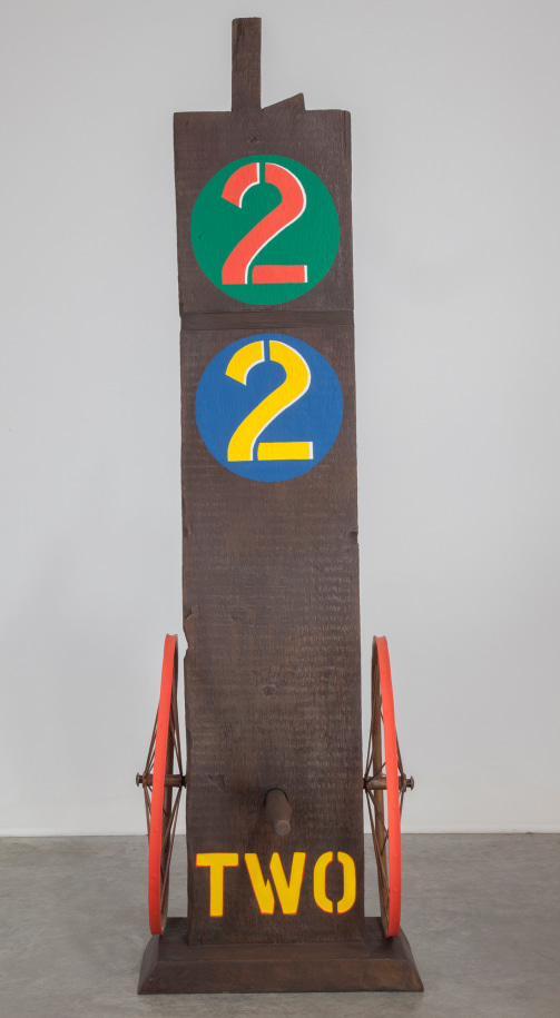 A 61 1/8 by 18 1/2 by 19 1/2 inch painted bronze sculpture of a beam with a haunched tenon, on a base. The work's title, &quot;Two,&quot; is painted in yellow stenciled letters across the bottom front of the sculpture. A wheel is attached to the bottom left and right sides of the sculpture, and a peg has been affixed to the front of the sculpture, in between the wheels. At the top of the sculpture is a green circle with a red numeral two, and below that is a blue circle with a yellow numeral two.
