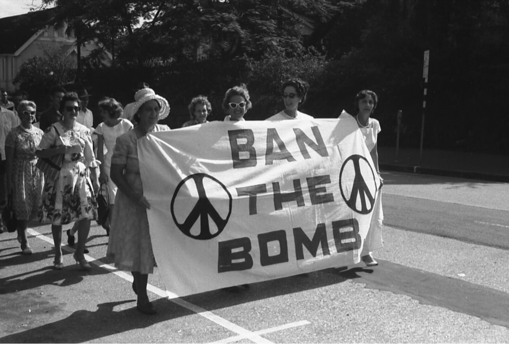 A Ban the Bomb march, led by four women holding a Ban the Bomb banner with peace signs