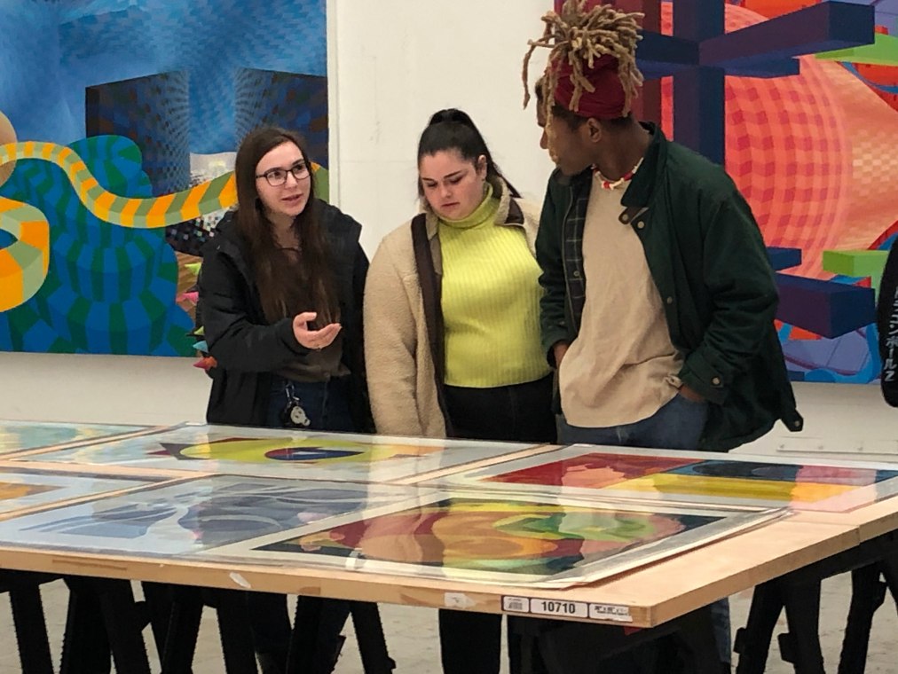 Three students discuss colorful abstract prints and paintings by Al Held.