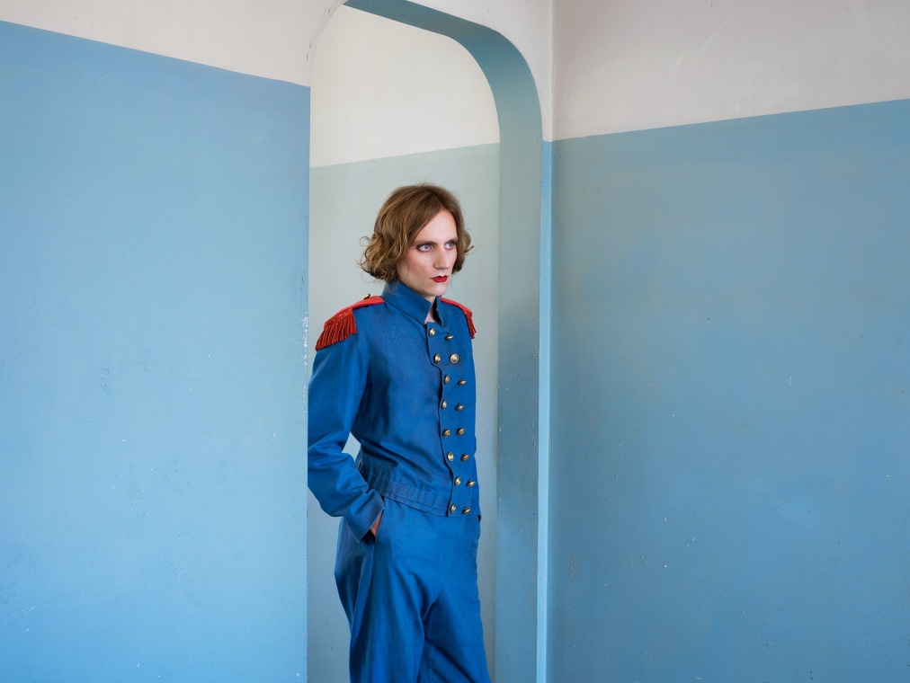 A person wears a blue uniform while standing in a room that is painted light blue.