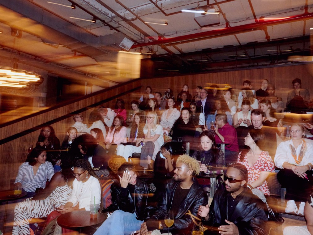 The lively interior of NeueHouse NY with people sitting on their packed indoor steps.