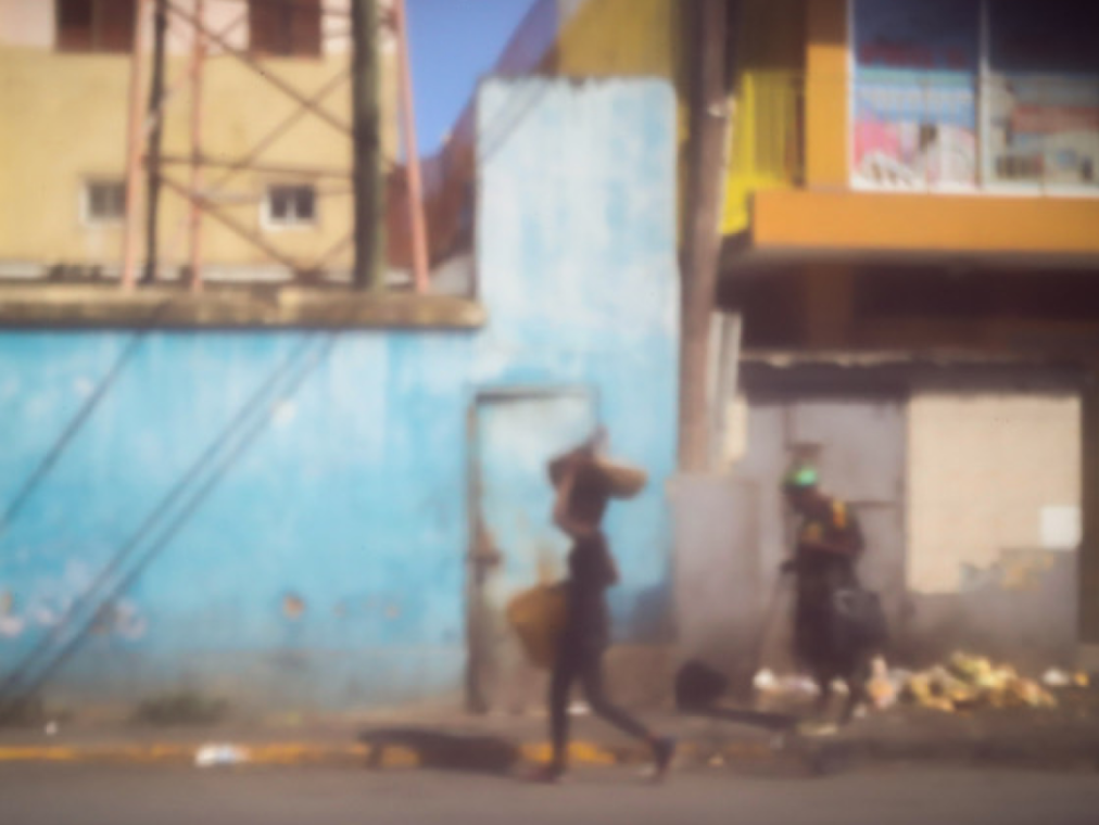 A blurry but colorful street scene with people walking in front of colorful buildings.