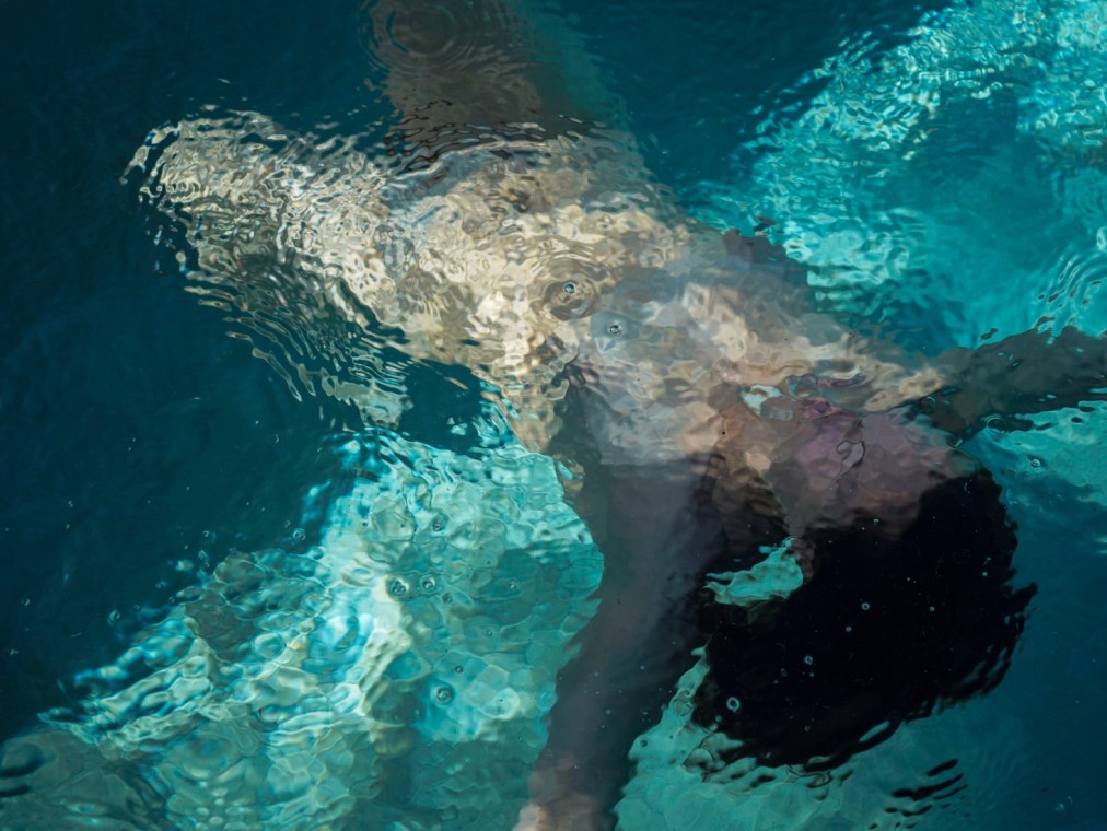 A naked woman floats in a pool and her body is abstracted by the moving water