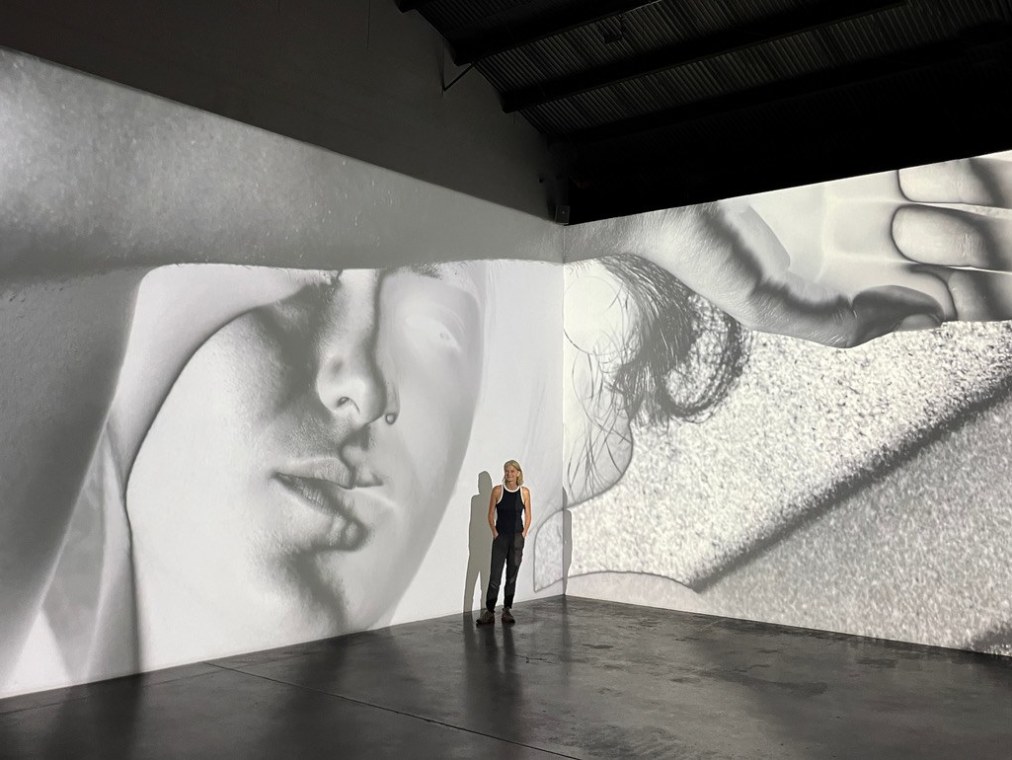 Artist Mona Kuhn stands inside her multi-wall installation where her photographs are projected onto gallery walls.