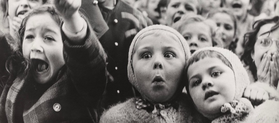 Black and white photo of a crowd of children reacting with excitement and astonishment.