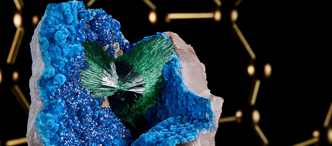 A fine mineral photograph of Malachite with a brass molecular model of malachite in the background.