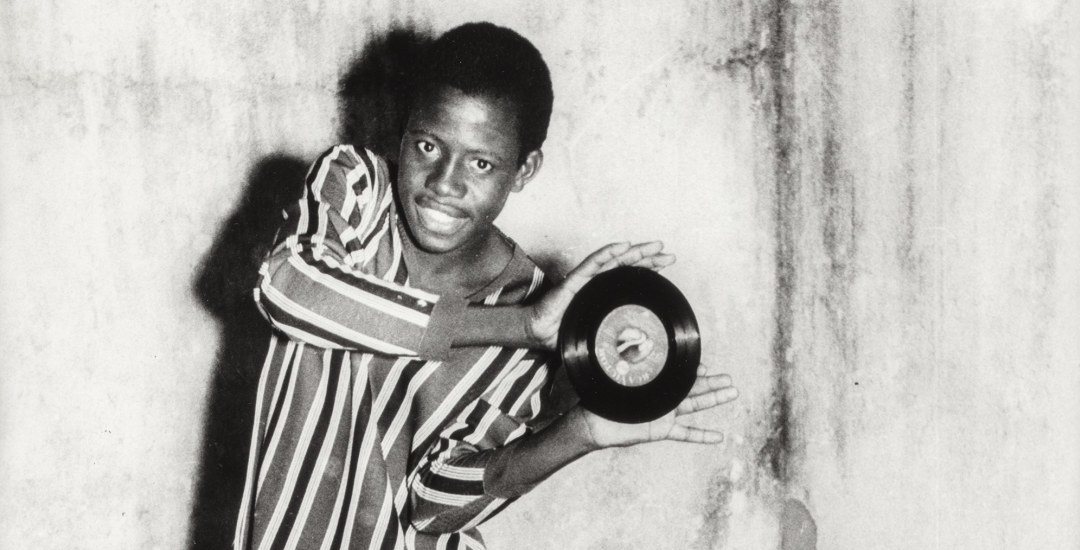 Black and white photo of a Black man posing with a 45 rpm record.