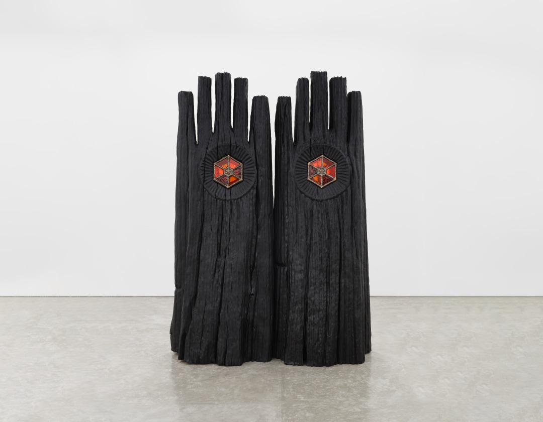 A totemic wooden sculpture two large joined hand like shapes with red and orange stained glass windows. 