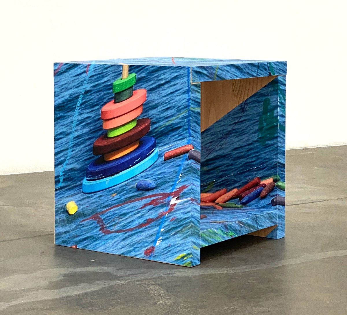 A stool wrapped in a photograph of water with toys and chalk