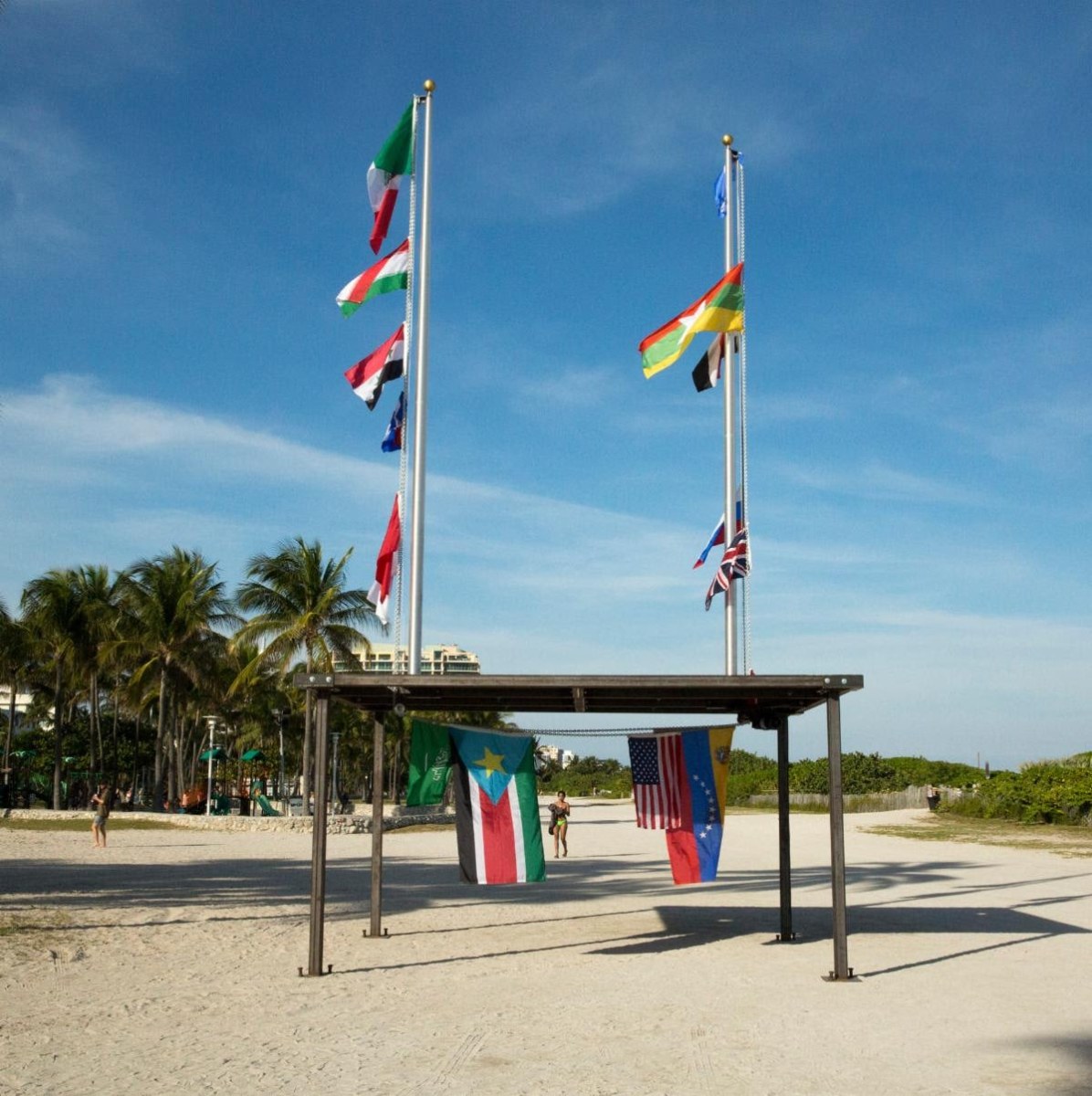 A large public sculpture on Miami Beach by Antonia Wright and Ruben Millares consisting of two flagpoles on a large steel platform. A motorized chain pulls flags from different countries up the poles and below the platform in a continuous motion.