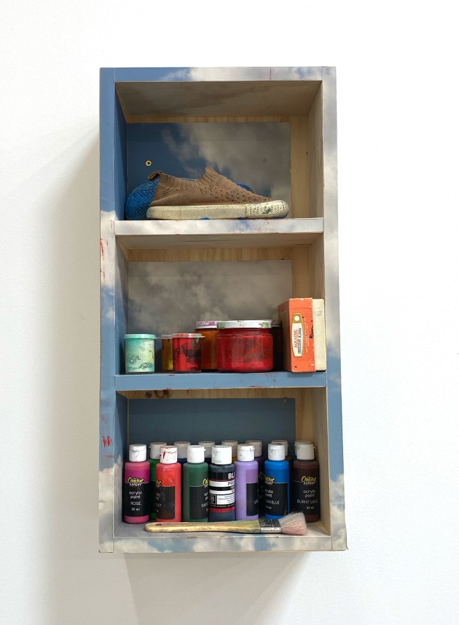 A shelf wrapped in a photograph of clouds and filled with paint and a pair of shoes