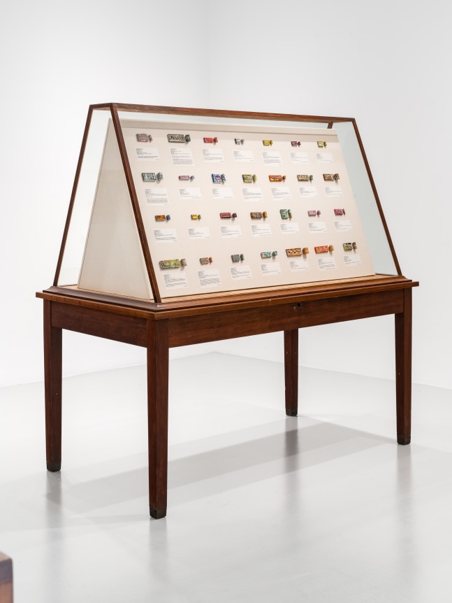 The invisible enemy should not exist (Vitrine 3 - cylinder seals), 2023, Glass vitrine, Middle Eastern food packaging and newspaper, glue