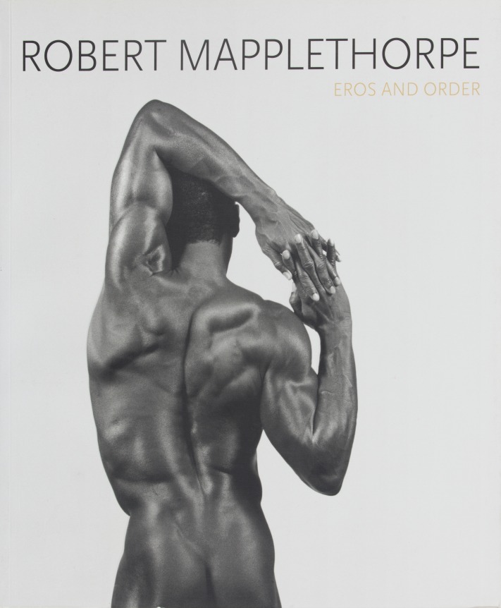 Figure study of a black man photographed from behind with one arm raised overhead, and fingers inter-laced.  Black and gold text at the top of the page.