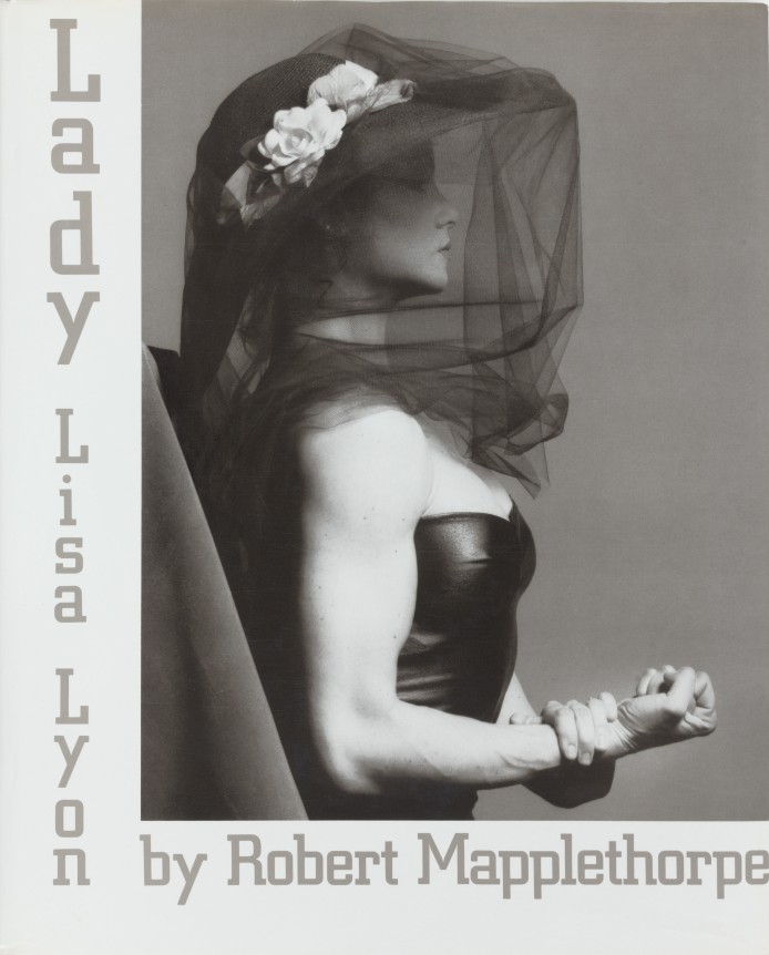 Lisa Lyon in profile, making a fist, wearing a black veil. Great text on white ground.