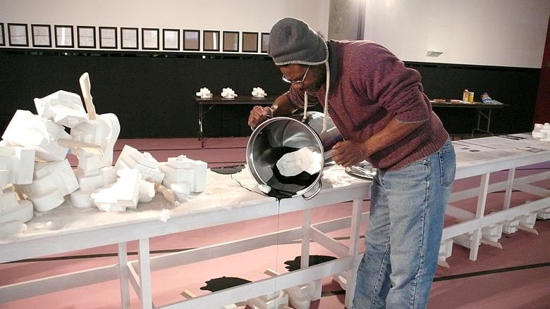 Pope.L pouring black liquid to create &quot;Performance Table&quot; installation