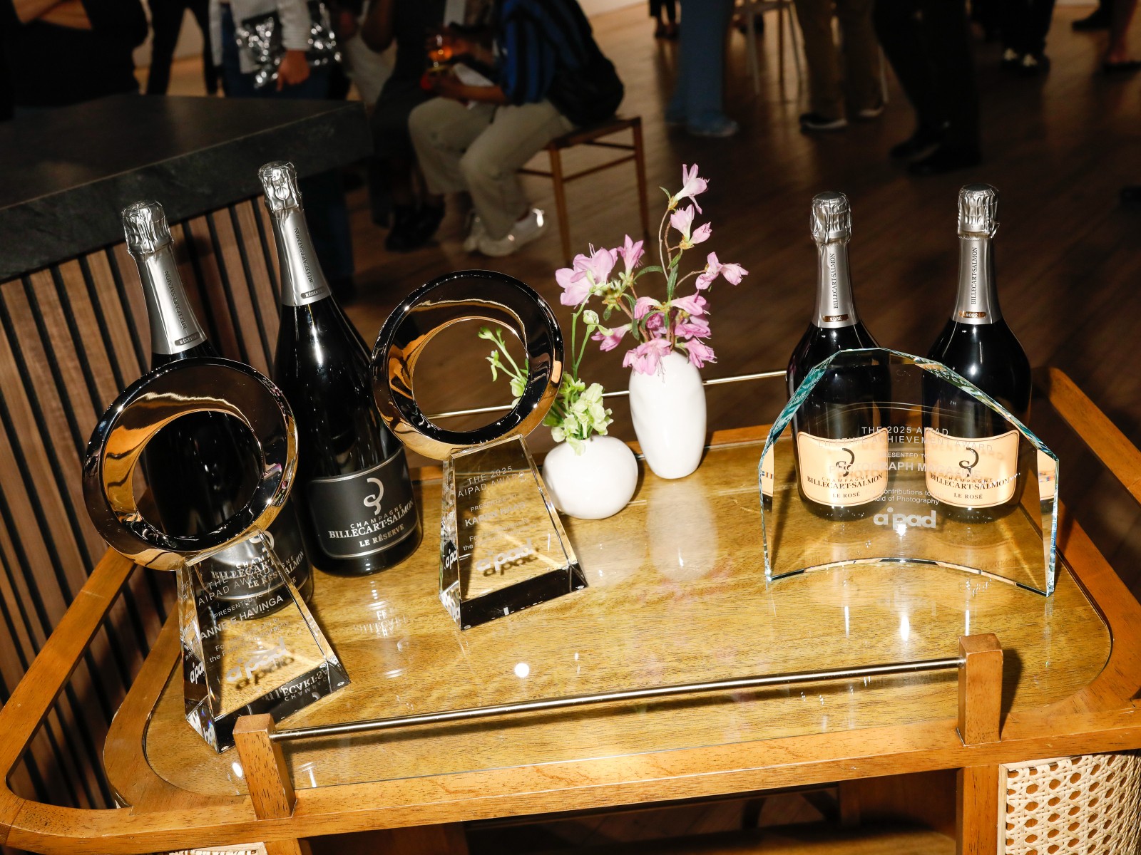 Bottles of champagne sit on a cart with the AIPAD Awards and two small vases of flowers.