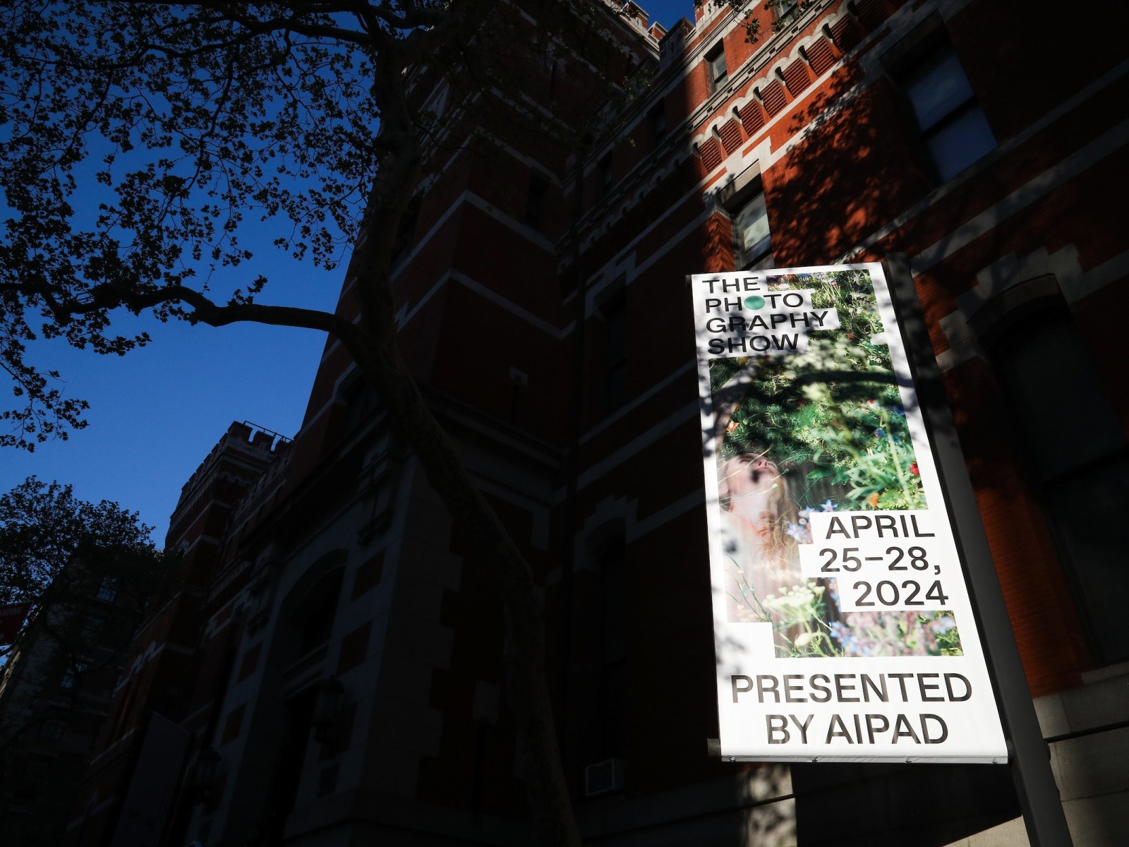 The front of the Park Avenue Armory the venue for 2024's iteration of The Photography Show, with a colorful banner and tree up above.