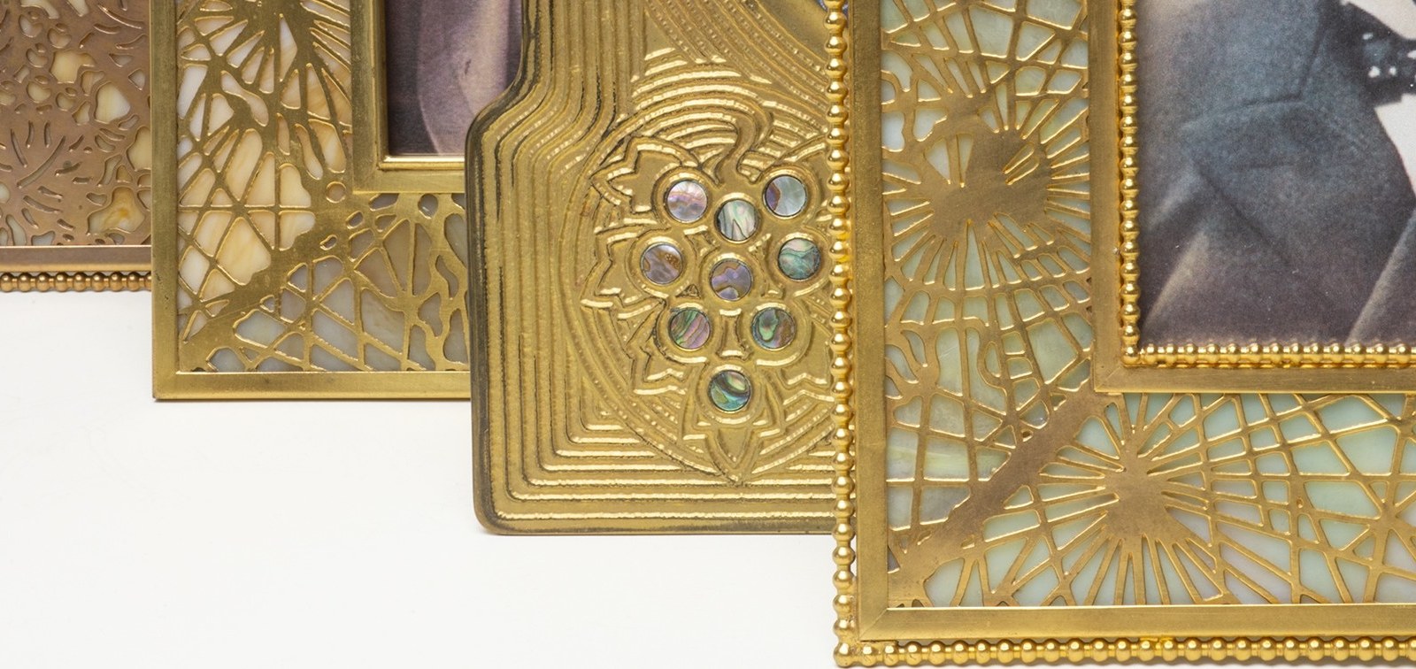 a detail shot showing close ups of bronze Tiffany Studios picture frames, some with mottled tiffany glass mounted with filigree of Pine Needles or Grapevines, another with inset abalone discs