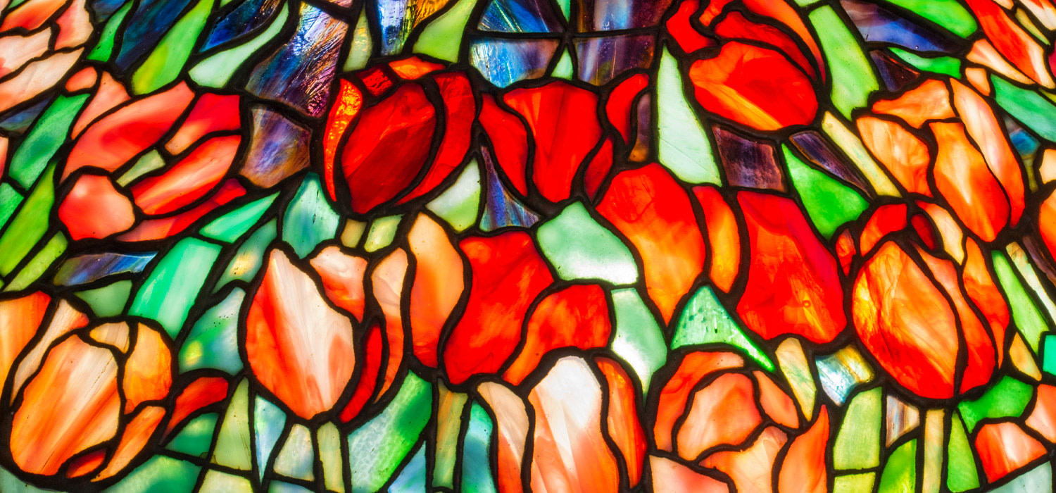 a close up detail of a leaded glass tulip shade for a tiffany lamp, the tulips formed by deeply saturated red tiffany glass streaked with white, with green petals, against a background glass in deep purple