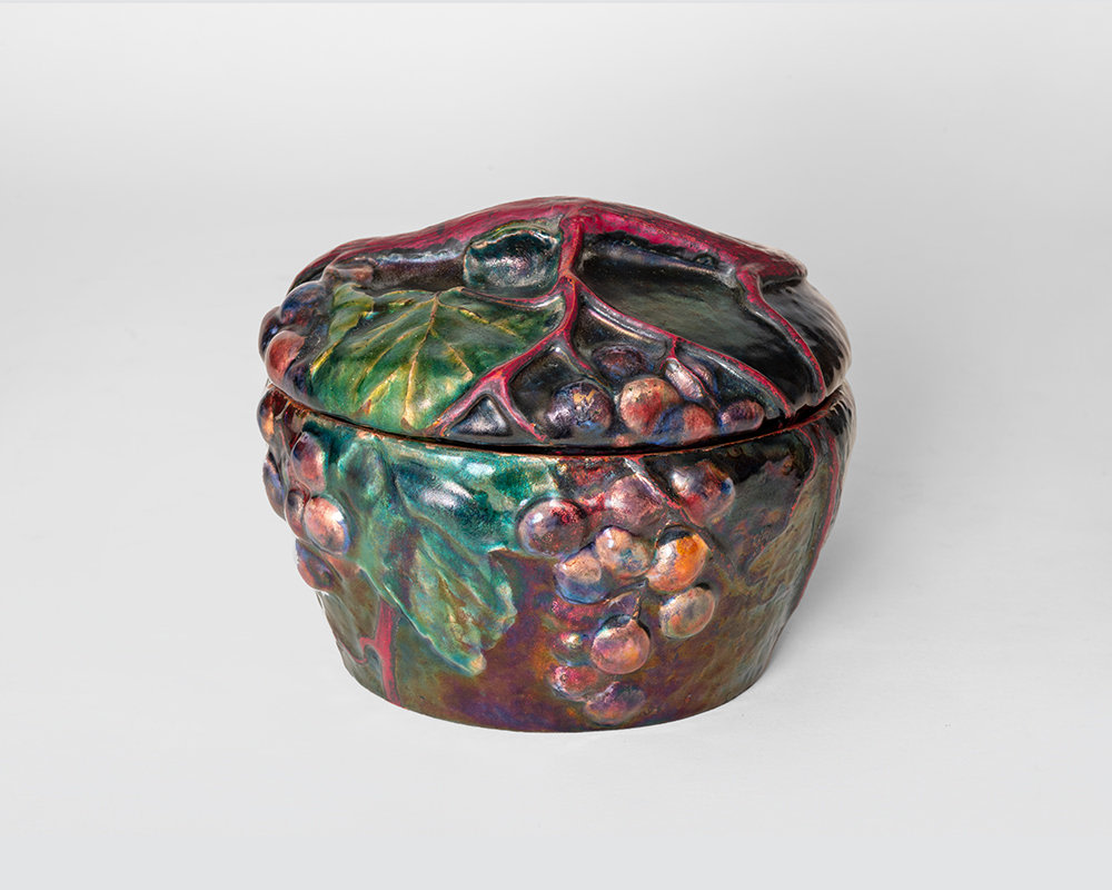 a rare enamel on copper lidded box by tiffany studios, depicting luminous clusters of iridescent grapes against a dark background