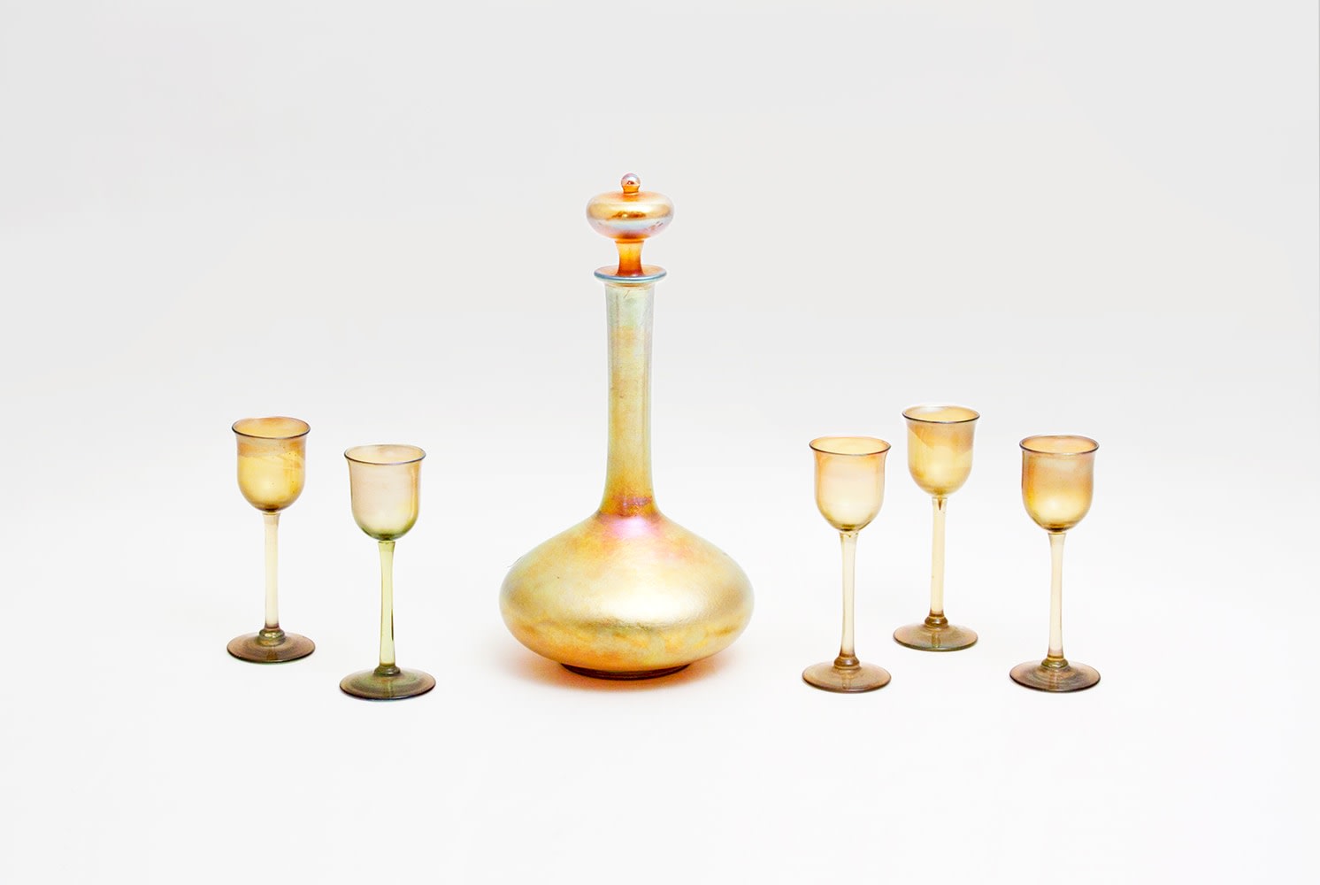 a gold iridescent favrile glass decanter with five small liqueur glasses by tiffany studios