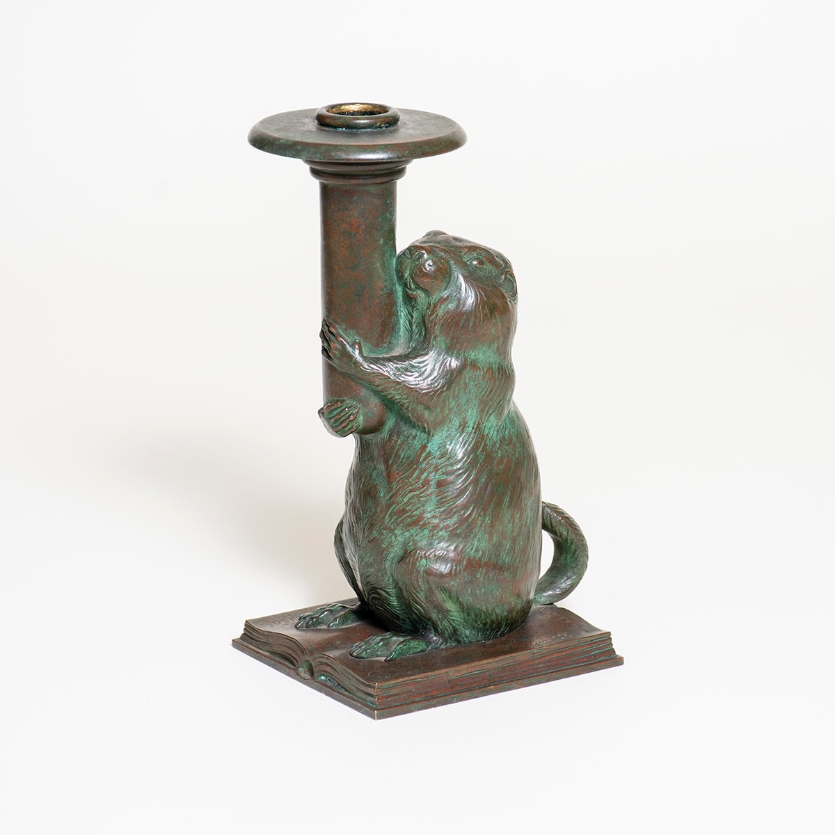 a bronze candlestick in the form of a groundhog standing on an open book, holding aloft the candle holder, by tiffany studios for the rowfant cub a cleveland bibliographic society