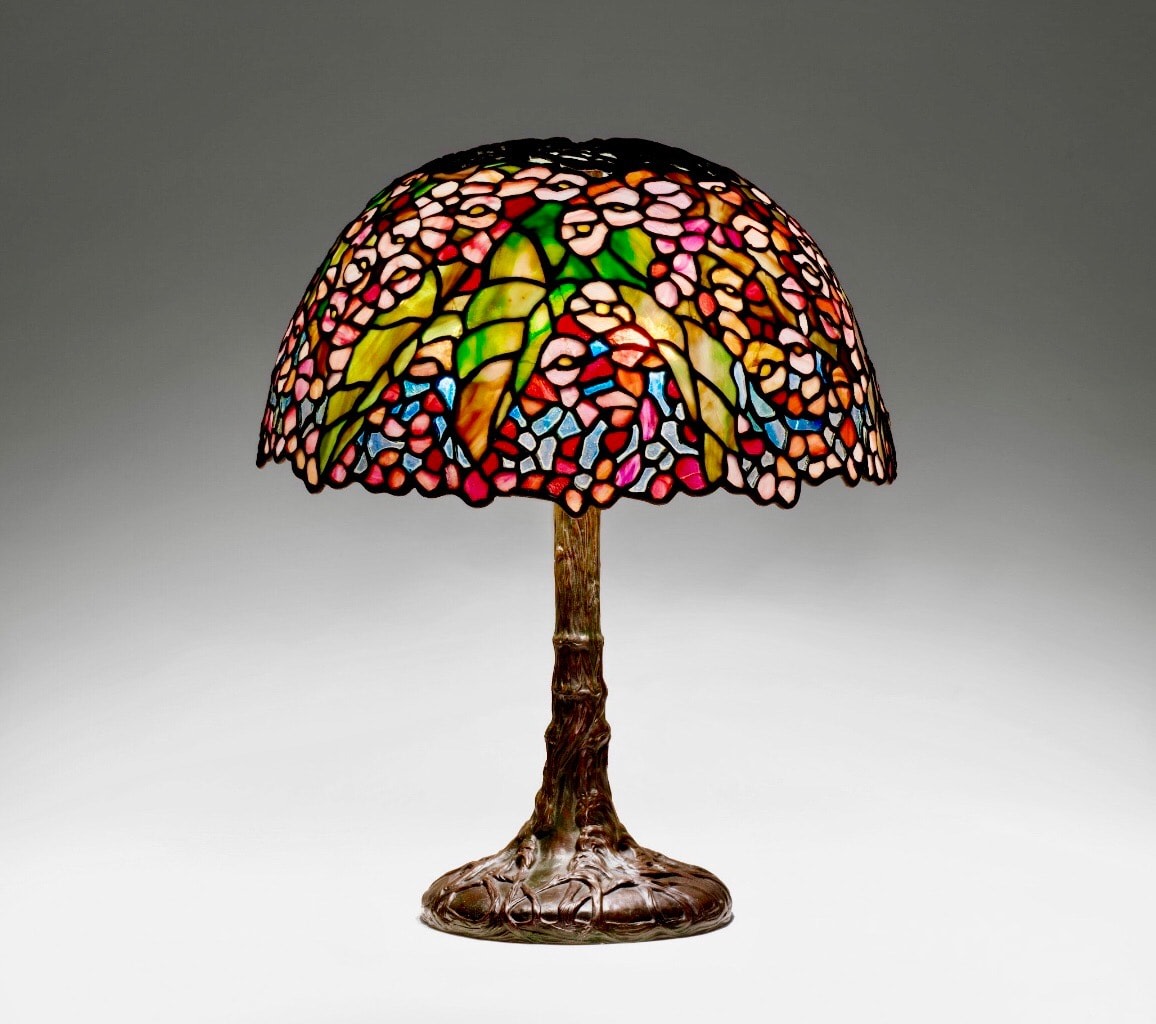 a tiffany studios pony begonia lamp, small in scale, the bronze tree-like base supporting a leaded glass shade depicting pink flowers against a clear glass sky in leaded tiffany glass