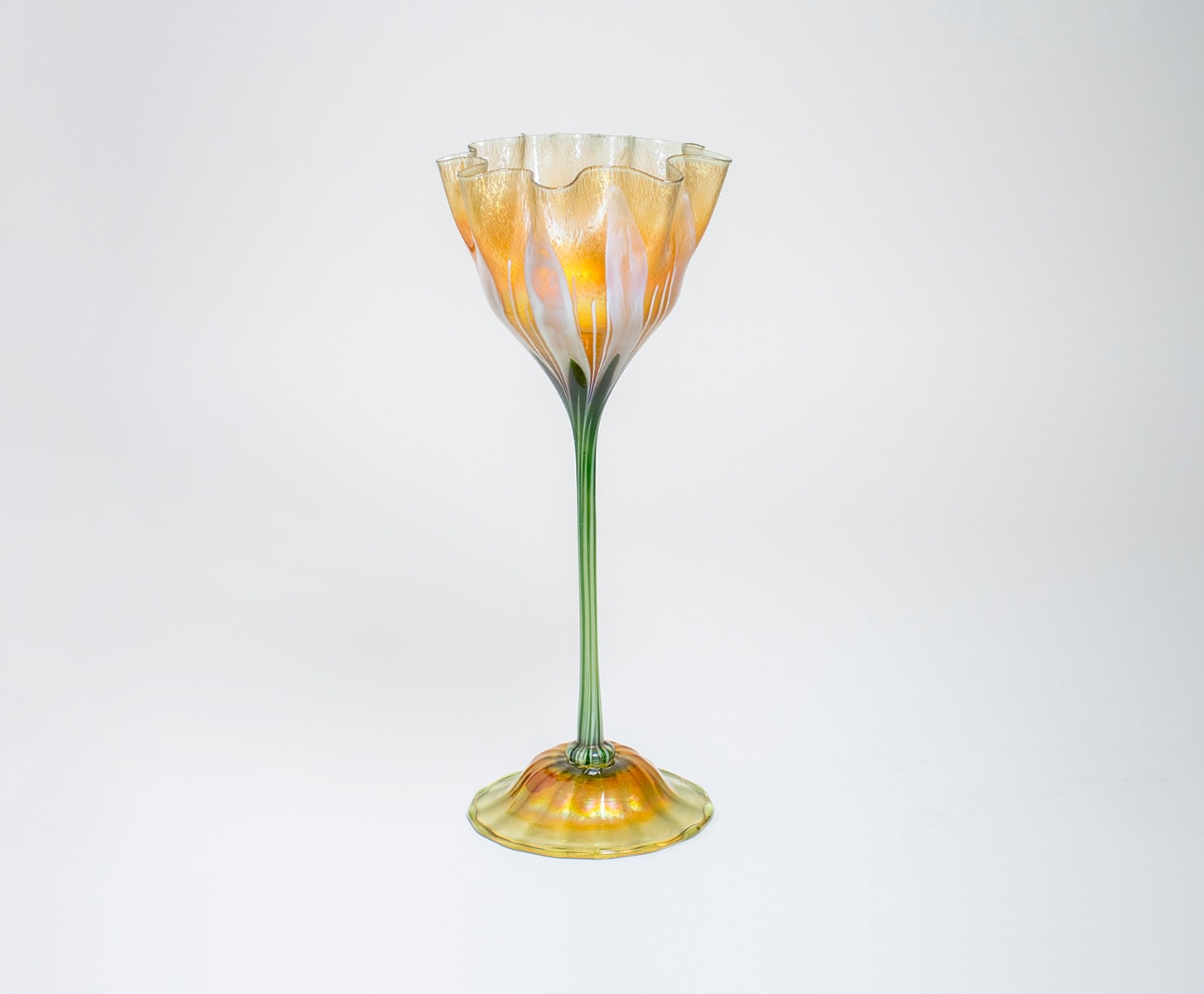 a tiffany favrile glass flower form, made by tiffany studios around 1900, a glass flower with thin green and white striped stem, the flower cup in gold iridescent glass with white stripes representing petals, the rim sculpturally ruffled