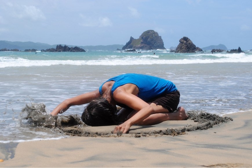 Woman on the beach in a circle of sand with her arms stretched forward.