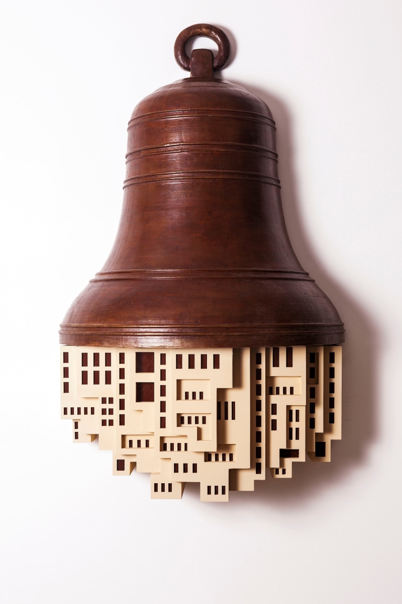 Large bronze bell with plastic buildings sticking out of the bottom.