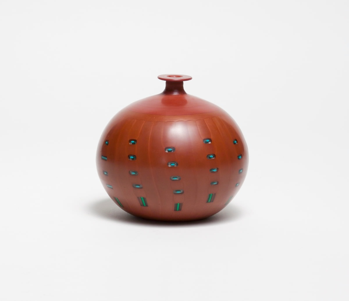 a blown glass vase made in murano by japanese artist yoichi ohira, the round body in a deep red clay color, with embedded clear bubble-like decorations in regular columns and rows each with a tiny inclusion of turquoise