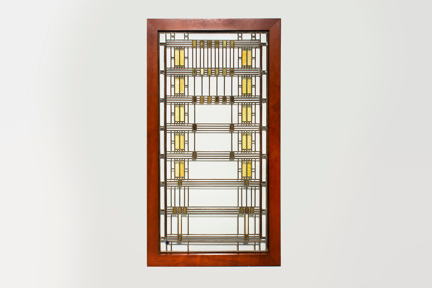 A leaded glass window in the Prairie style by Frank Lloyd Wright, the vertical rectangular window depicting rectilinear stylized depiction of wisteria panicles in iridescent yellow glass against a clear background allowing you to see through the panel