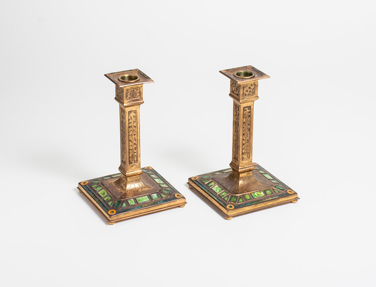 a pair of bronze candlesticks by louis comfort tiffany furnaces inc in the &quot;art deco&quot; pattern known for rectilinear recessed decoration filled with enamel, in this example the enamel is variegated green
