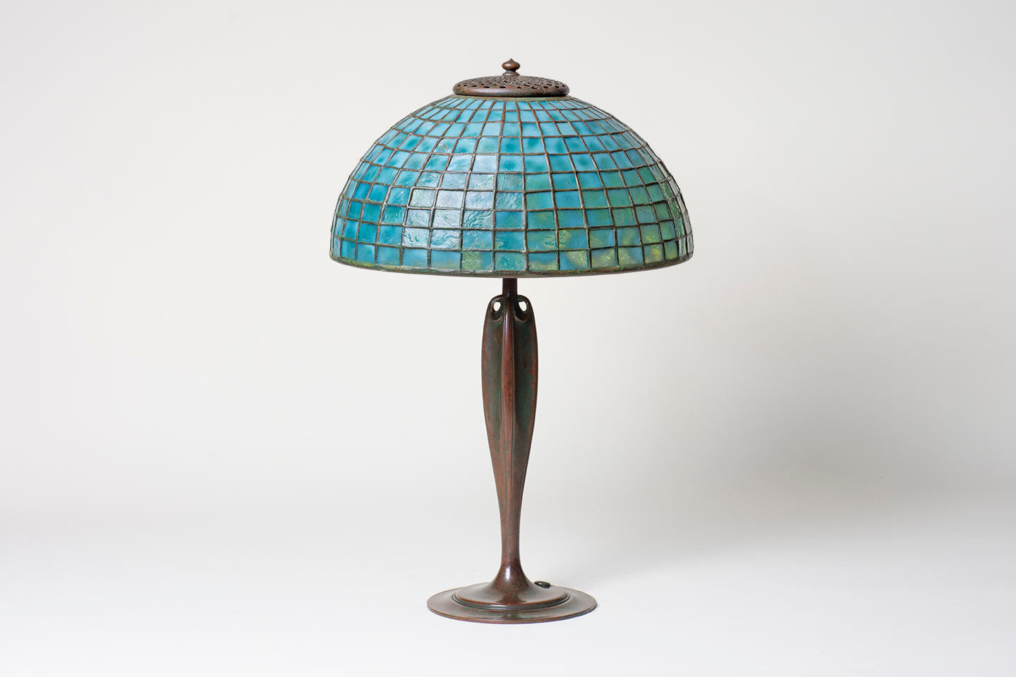 an authentic Tiffany Lamp dating from the early 20th century, pictured unlit, with an elegant Art Nouveau style bronze base in rich brown patina, supporting a dome-shaped leaded glass shade formed by square shaped pieces of mottled blue Tiffany Glass