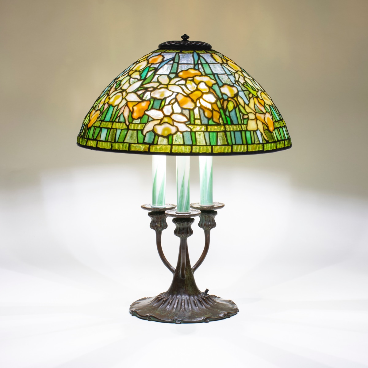 a leaded glass tiffany lamp depicting sunny mottled yellow daffodil flowers with spiky leaves in shades of green to greenish blue against a transparent glass sky