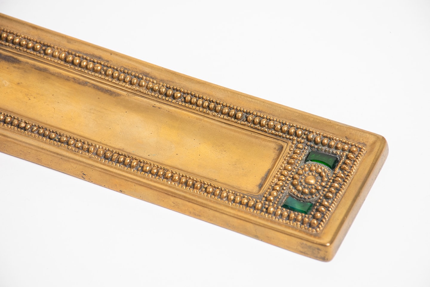 a gilt bronze tiffany studios pen tray from the byzantine pattern desk set, a rectangular piece with a central well for the pen, framed by a border of beadwork with inset pieces of tiffany favrile glass in a shade of emerald green