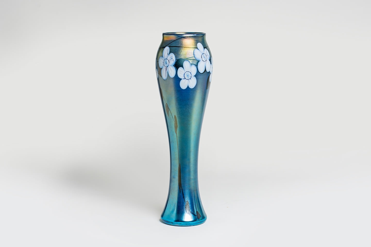 A monumental cylindrical tiffany favrile glass vase in iridescent blue, decorated at the rounded shoulder with a design of large white flowers and green leaves, the white flowers with wheel-carved details including curled petals