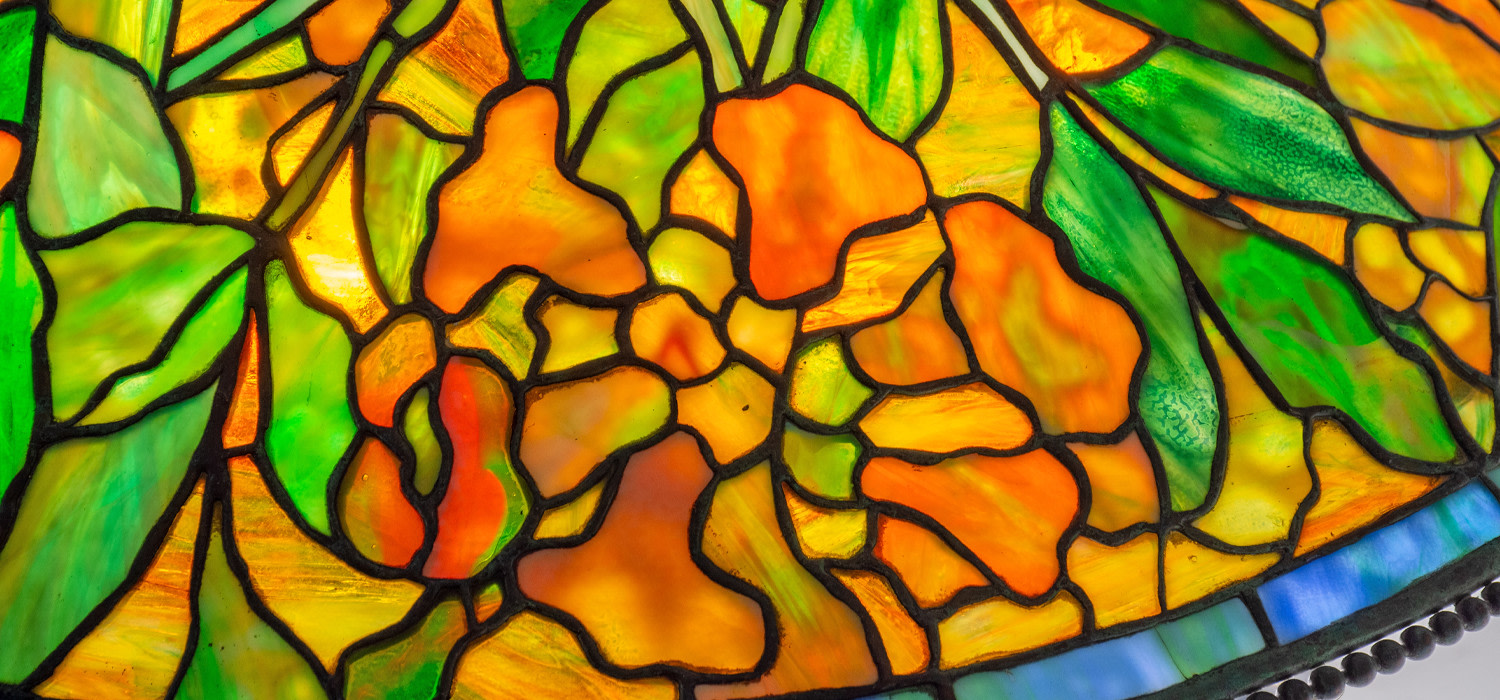 A detail of an original antique tiffany lamp, depicting in leaded glass orange trumpet creeper blossoms formed by mottled deep orange opalescent tiffany glass with bright green leaves