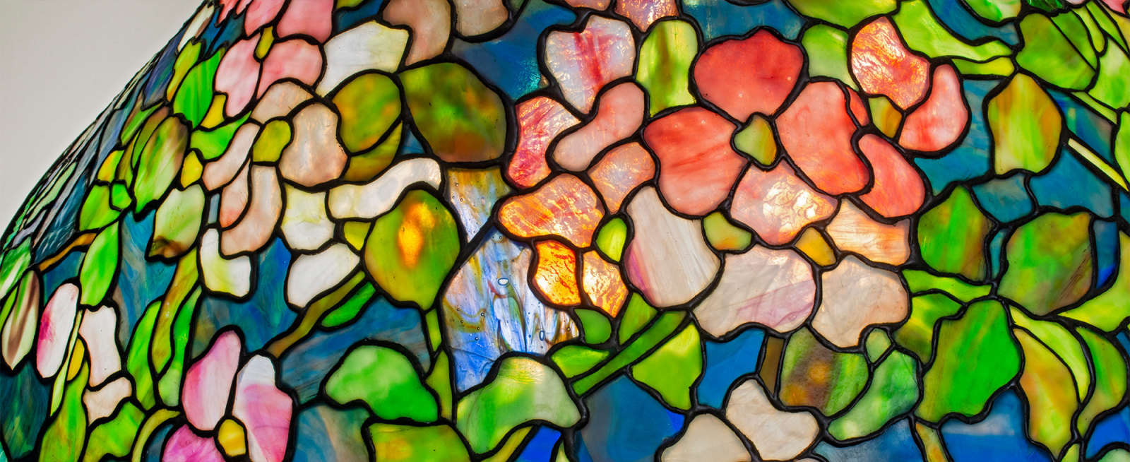 A detail of an original antique tiffany lamp, depicting in leaded glass pink and white four petaled dogwood flowers, with mottled green pointed leaves, against a background of opalescent deep blue tiffany glass