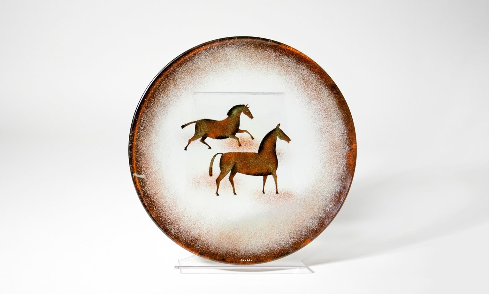 a shallow circular charger with mid-century stylized depiction of two brown horses, one galloping and one standing, by artist maurice heaton in his trademark technique using powdered enamel