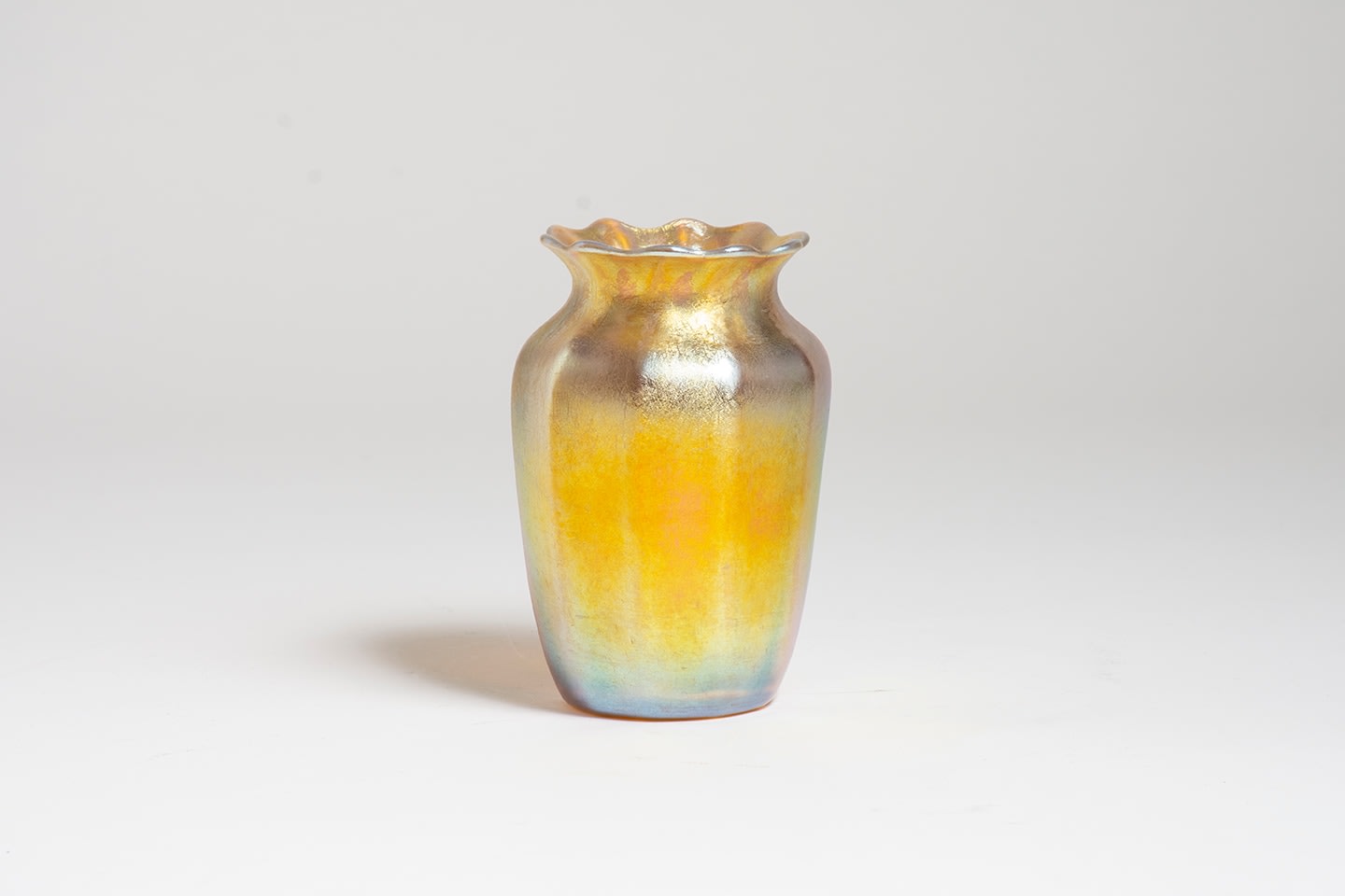 a gold iridescent tiffany glass vase with wide subtle vertical facets on the body as well as a scalloped rim