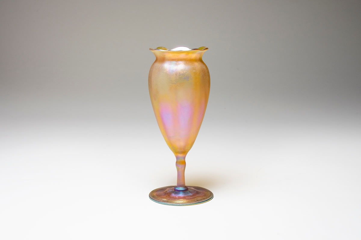 a gold iridescent tiffany favrile glass &quot;flower form&quot; vase, a narrow footed stem featuring an elongated flower cup with pinched and ruffled rim, imitating a flower in blown glass
