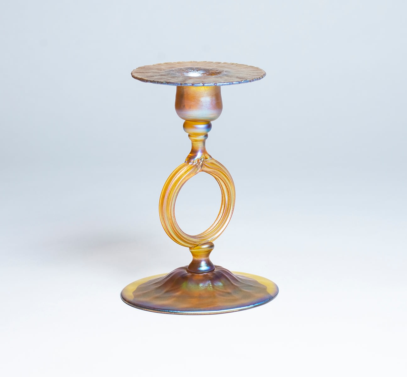 a gold iridescent Tiffany Favrile Glass Candle Stick, on a domed foot, with an open circular ring for the &quot;stem&quot; rising to support a flared candle cup.